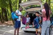 Two parents and two kids pulling backpacks out of a station wagon