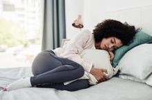 Woman curled up uncomfortably in bed