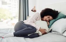 Woman curled up uncomfortably in bed