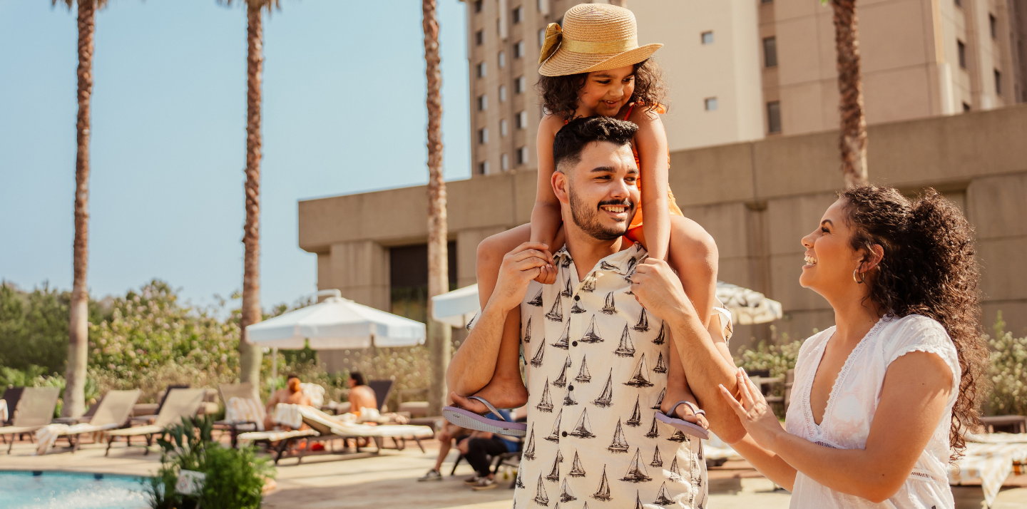 Couple with young daughter walking by hotel pool after looking for the best travel deals