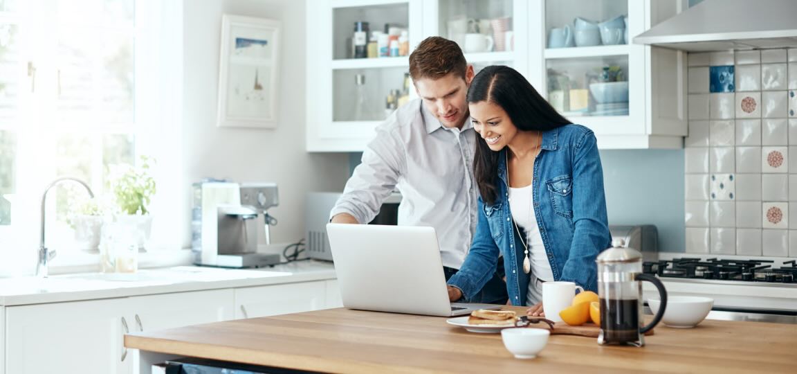 Couple on a laptop in the kitchen figuring out how to calculate trip cost for a travel insurance policy