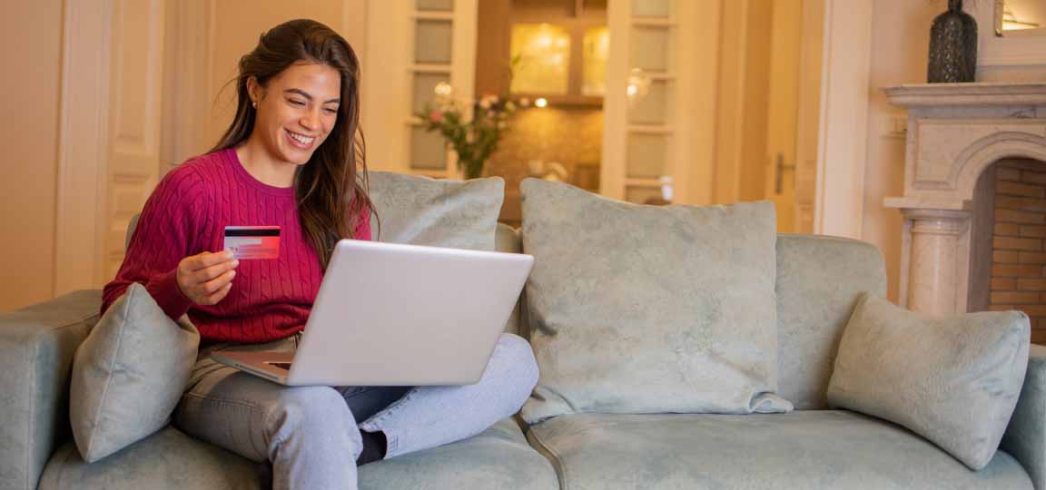 Young woman on her laptop and holding a credit card while wondering, "How much is travel insurance?" 