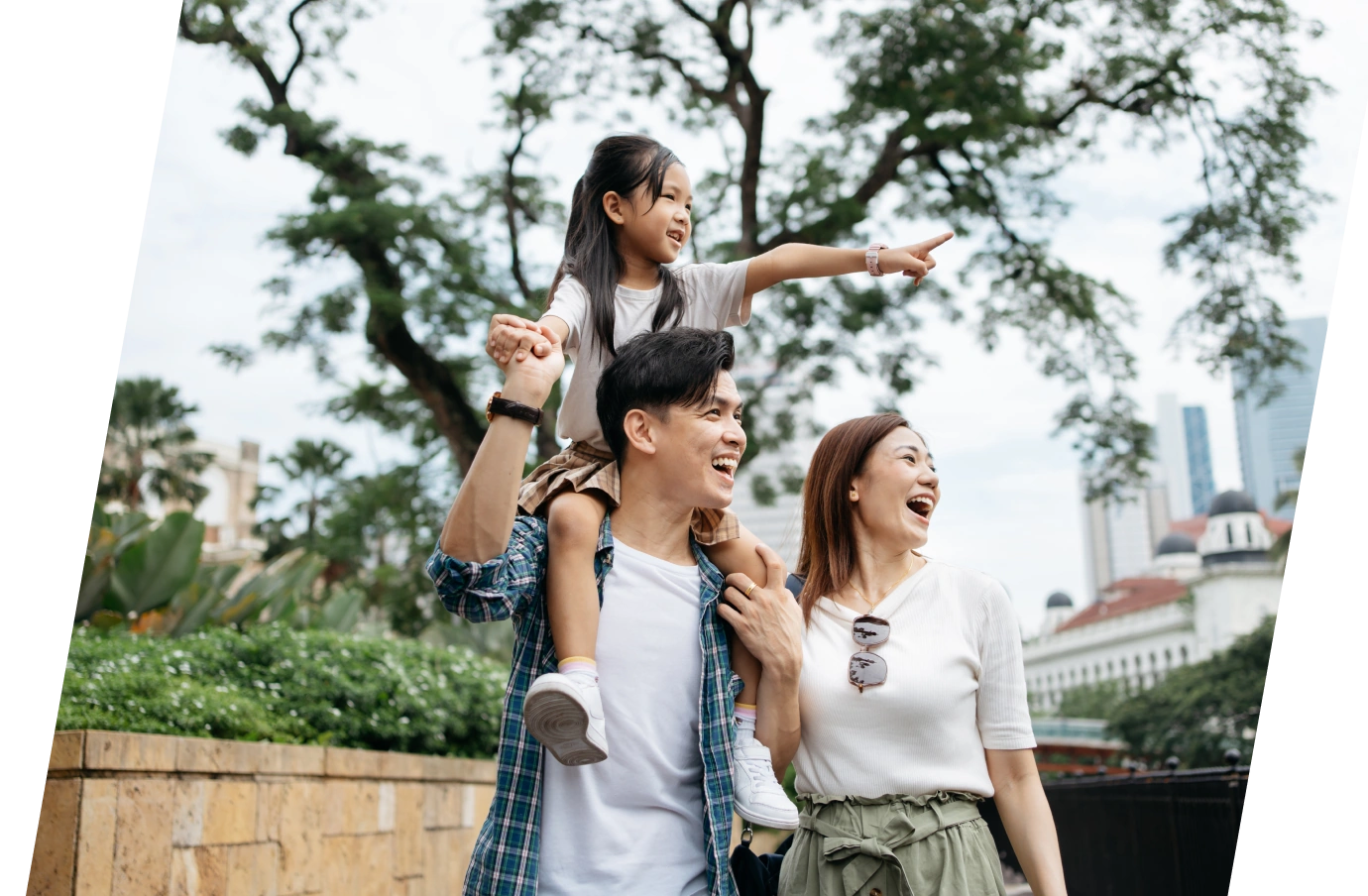 a man with travel insurance for city trips holds his daughter on his shoulders as they sightsee with his partner 