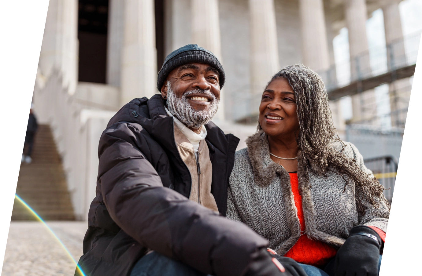 a black couple in winter clothes, sitting on city steps with smiles on their faces and travel insurance for Washington D.C. 