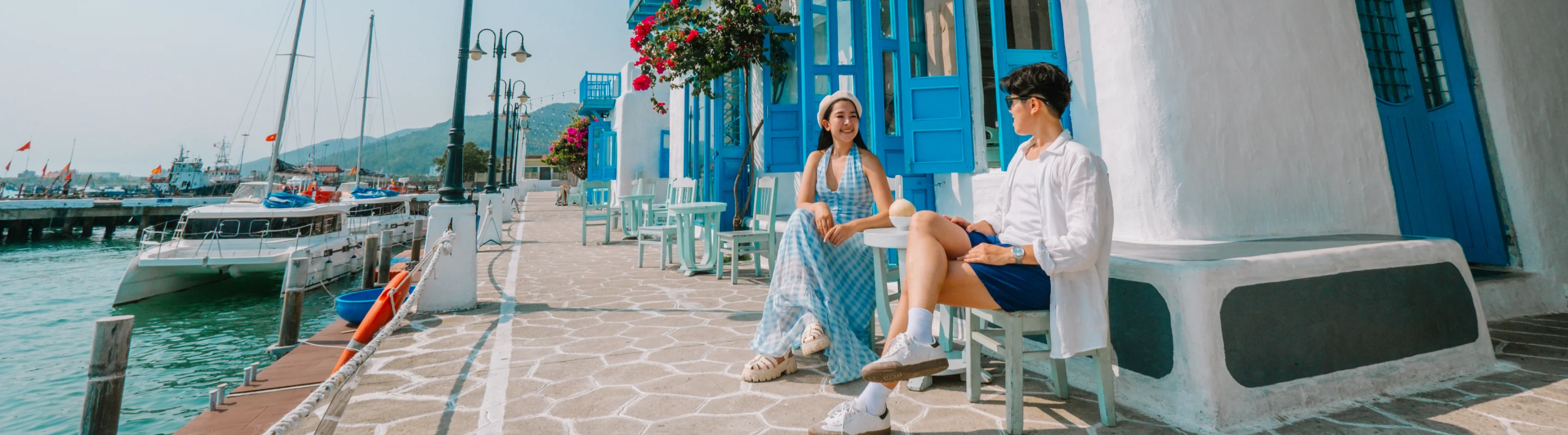 Young couple with travel insurance for Vietnam sitting at a small table outside of a blue and white building on a marina
