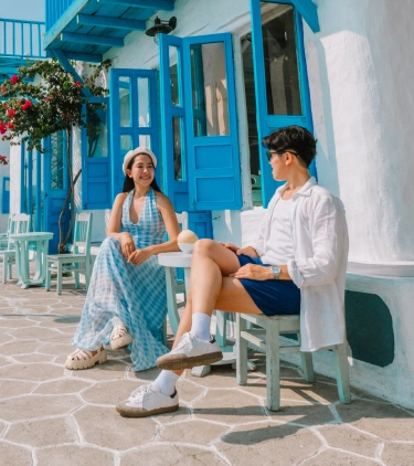 Young couple with travel insurance for Vietnam sitting at a small table outside of a blue and white building on a marina