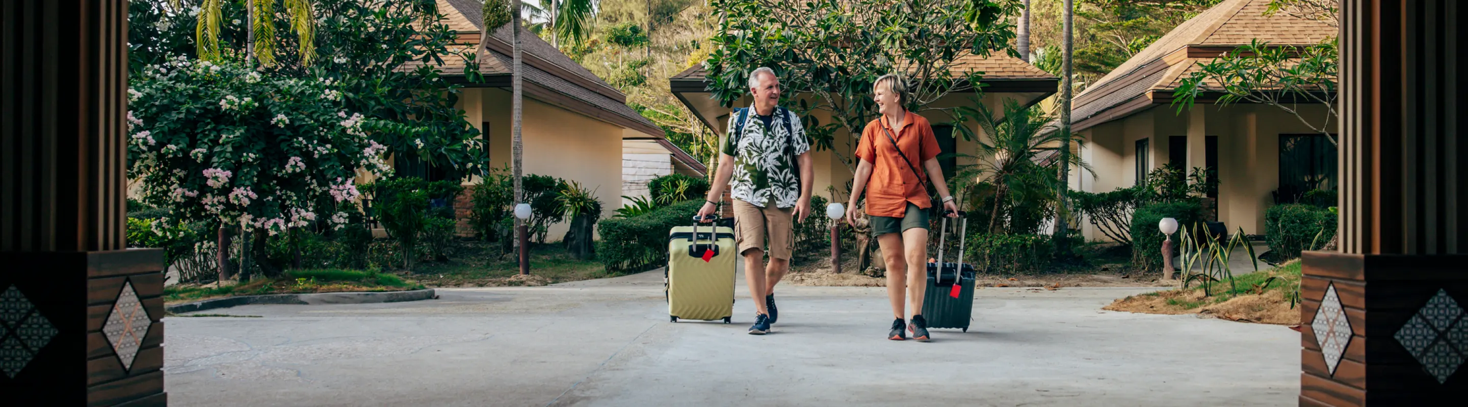 Middle-aged couple with travel insurance for Thailand, walking with suitcases at a resort