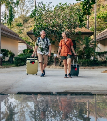 Middle-aged couple with travel insurance for Thailand, walking with suitcases at a resort
