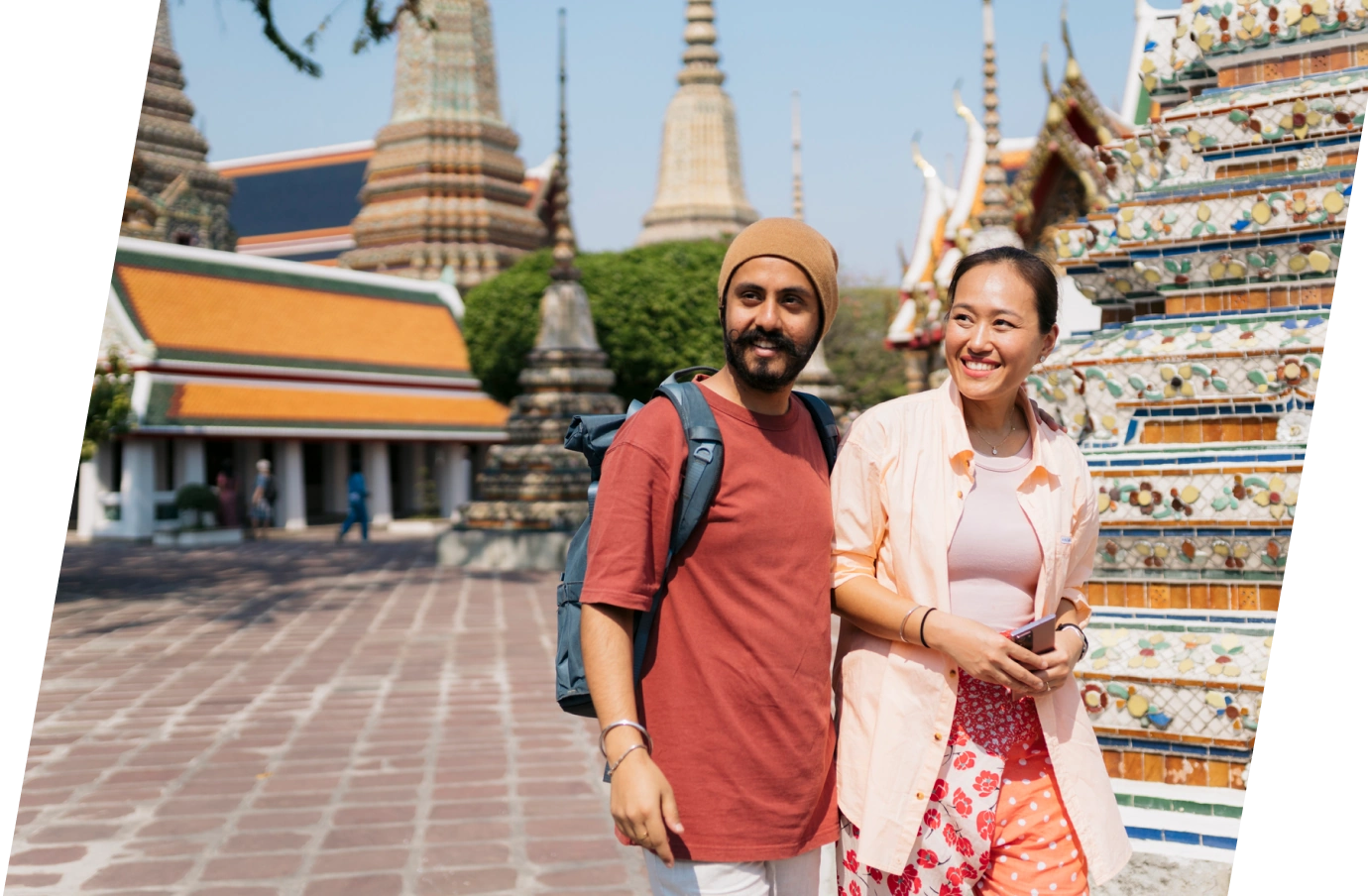 Young couple with travel insurance for Thailand, smiling and walking through a Thai temple on a sunny day