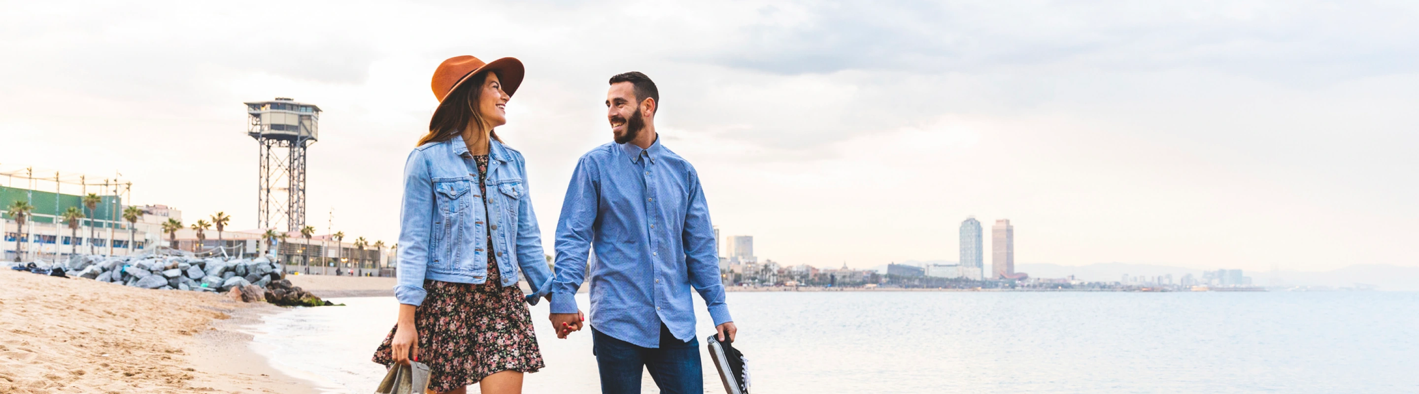 a couple with travel insurance for Spain, holding hands as they walk on the beach
