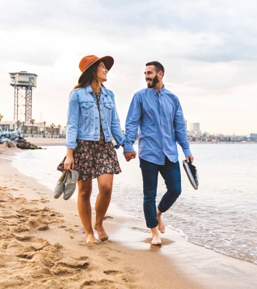 a couple with travel insurance for Spain, holding hands as they walk on the beach