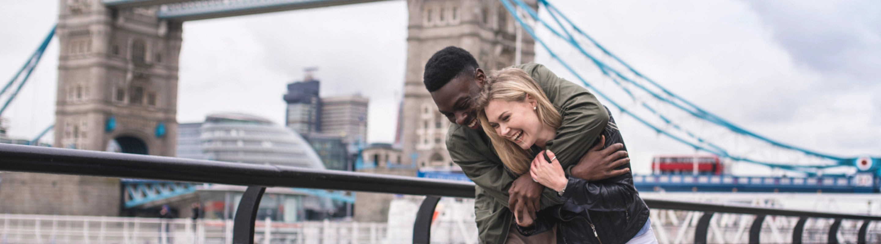 a couple with travel insurance for the United Kingdom, showing affection in front of the London Bridge