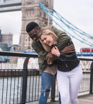 a couple with travel insurance for the United Kingdom, showing affection in front of the London Bridge