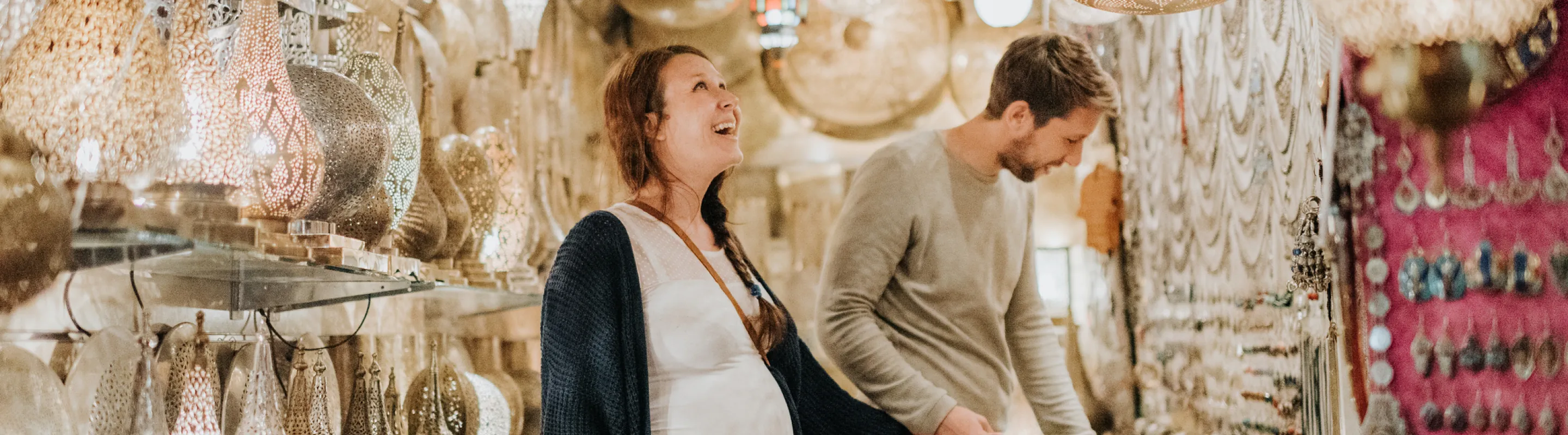 a young, expecting couple with travel insurance for pregnancy looks at hanging lanterns in a bizarre setting