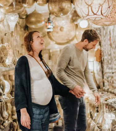 a young, expecting couple with travel insurance for pregnancy looks at hanging lanterns in a market stall in a bizarre setting