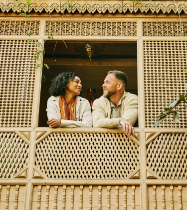 Couple with travel insurance plans smiling at each other on a balcony in Morocco
