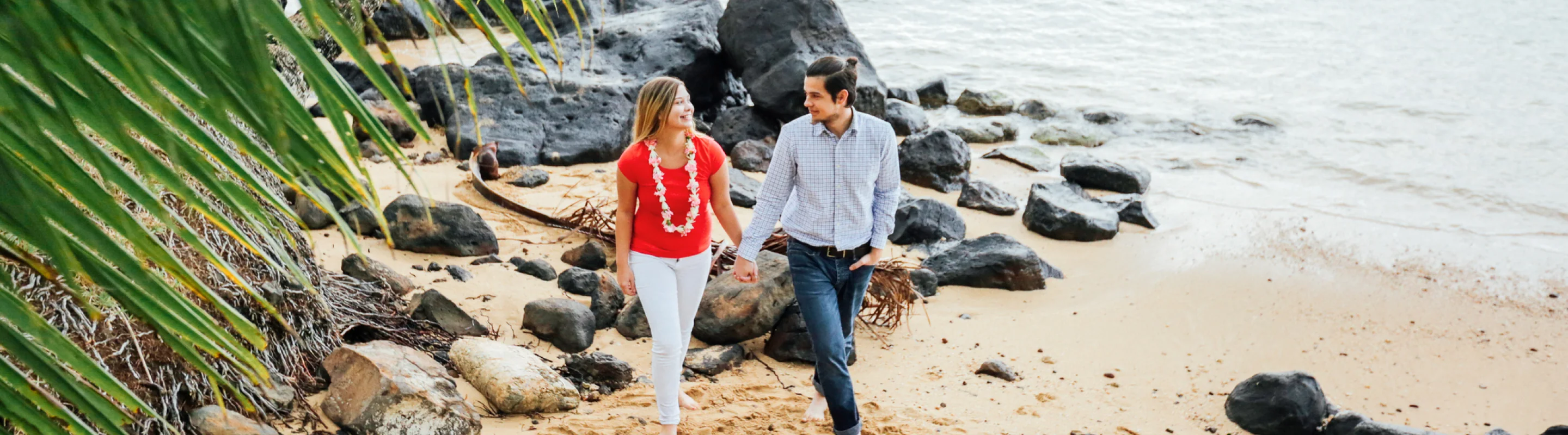 Couple with travel insurance for Hawaii holding hands and walking on a rocky beach