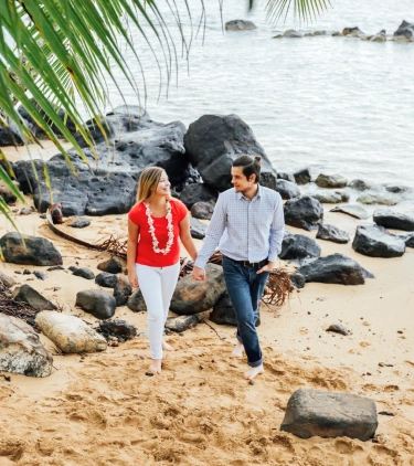 Couple with travel insurance for Hawaii holding hands and walking on a rocky beach