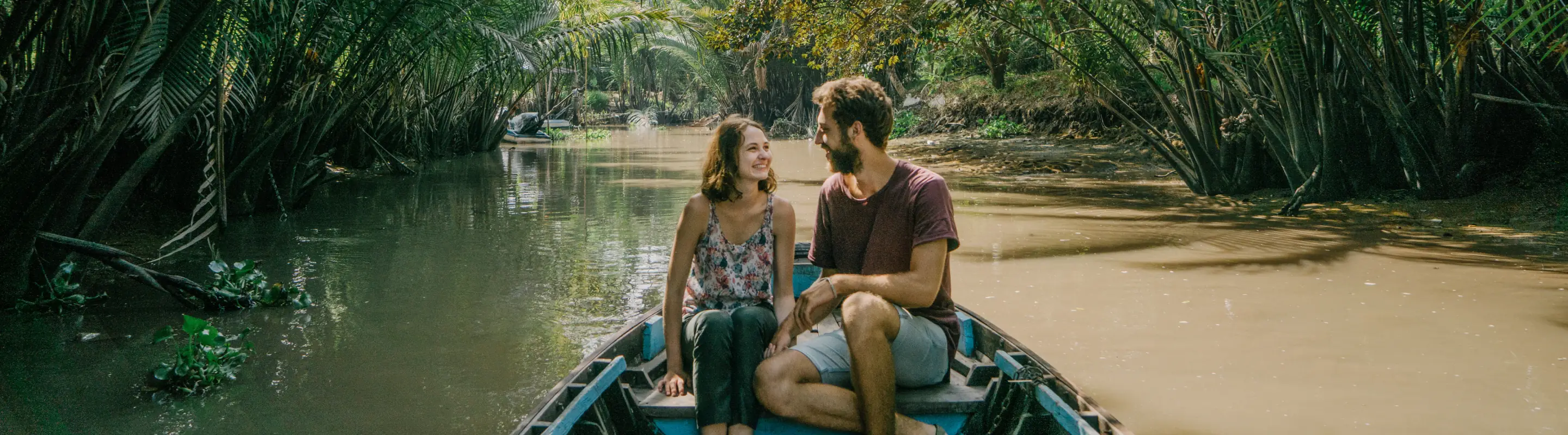 Couple with travel insurance for Vietnam on a small boat cruising through the jungle with trees overhead