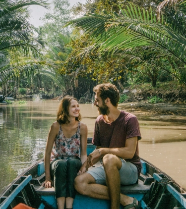 Couple with travel insurance for Vietnam on a small boat cruising through the jungle with trees overhead