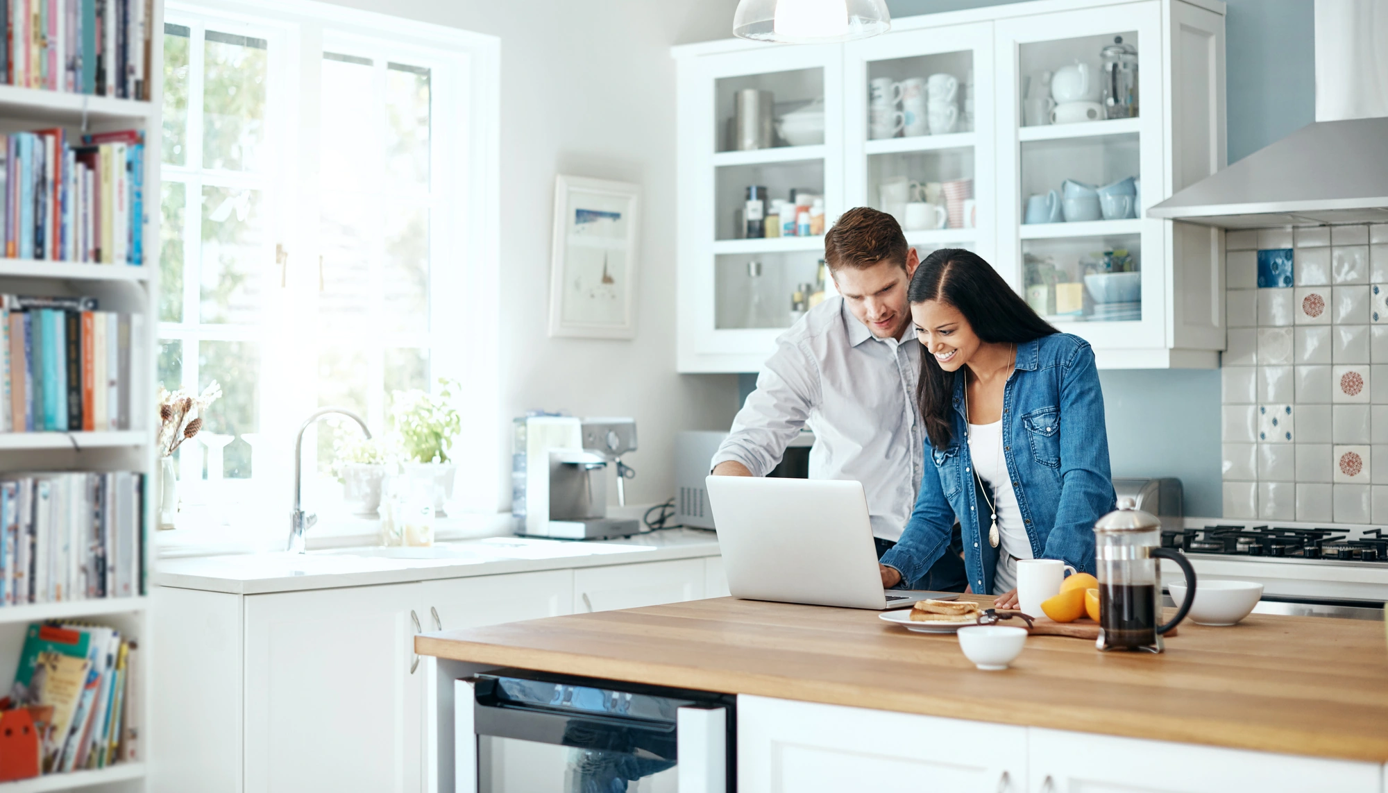 Couple using a laptop in their kitchen to calculate trip cost for their travel insurance policy