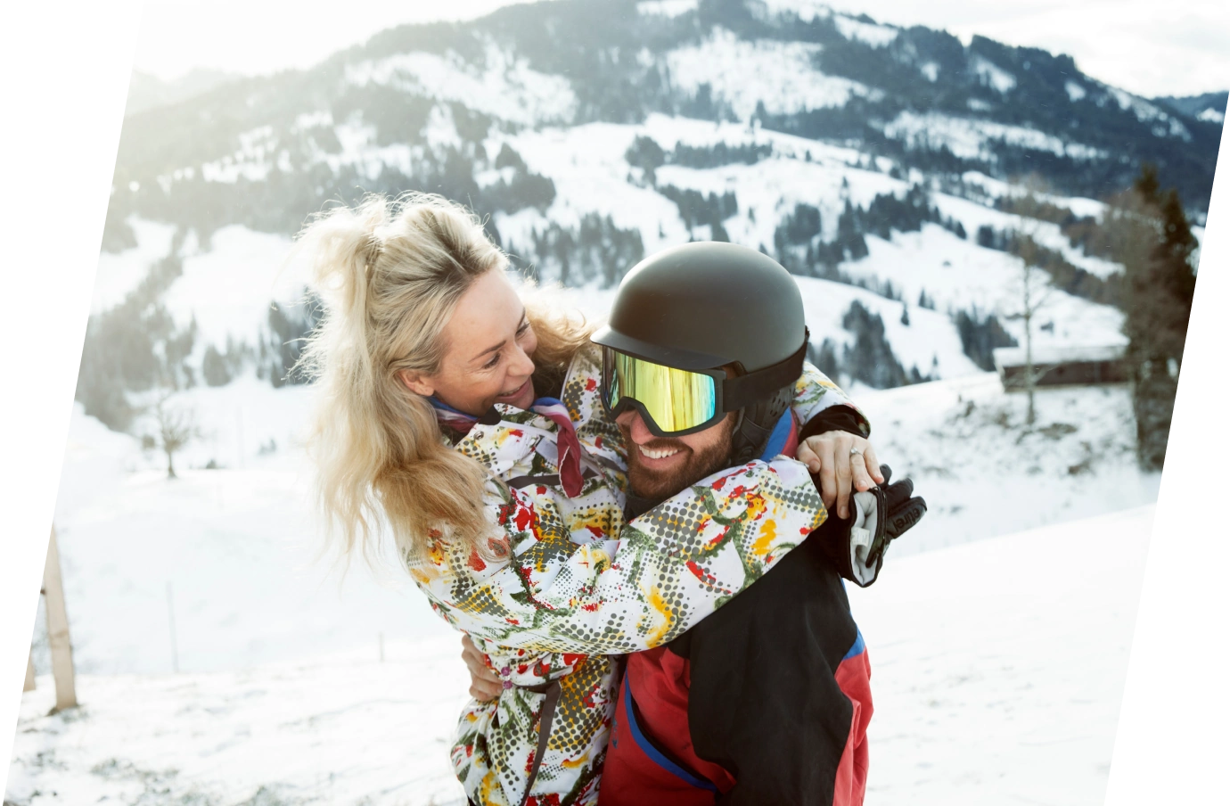 a couple with travel insurance for Switzerland hugs at the top of a mountain in ski attire on vacation