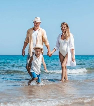 a couple with travel insurance for Egypt walk along the shoreline of an ocean while their son runs ahead
