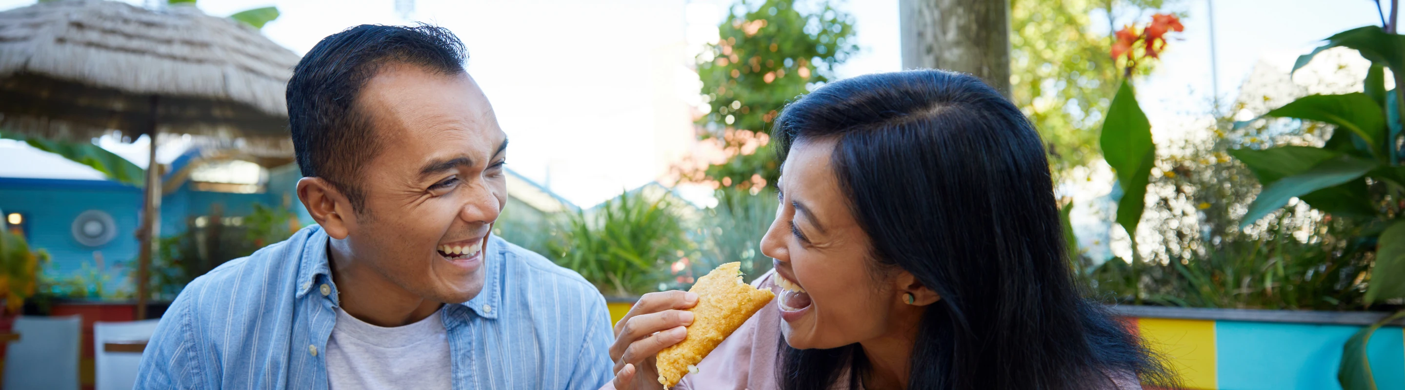 an Asian couple laughs and enjoys tacos at a colorful eatery, insured with travel insurance for city trips 
