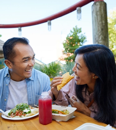 an Asian couple laughs and enjoys tacos at a colorful eatery, insured with travel insurance for city trips 