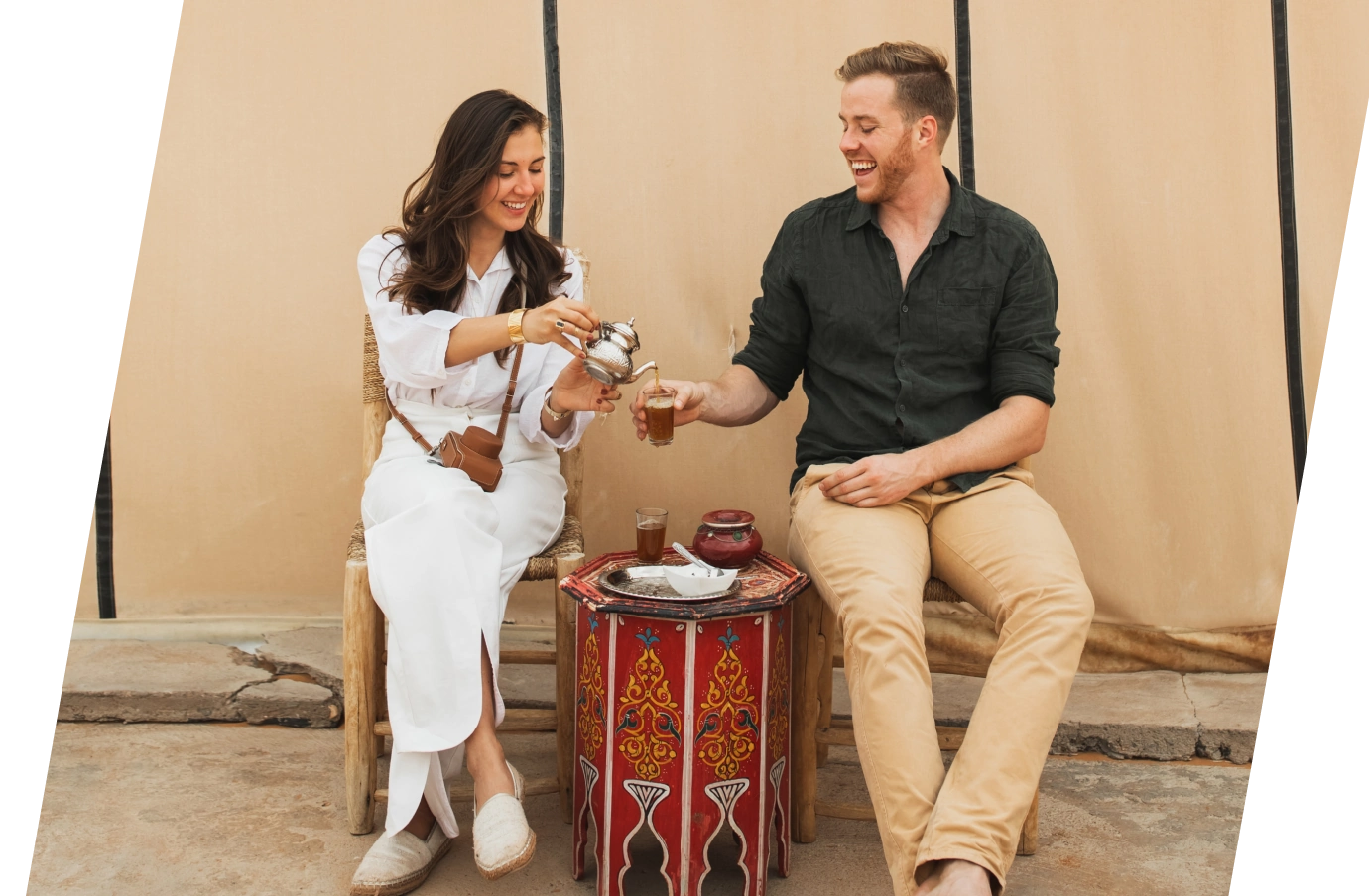 a young couple with travel insurance for the UAE smile as they drink tea at a traditional Emirati tea setup