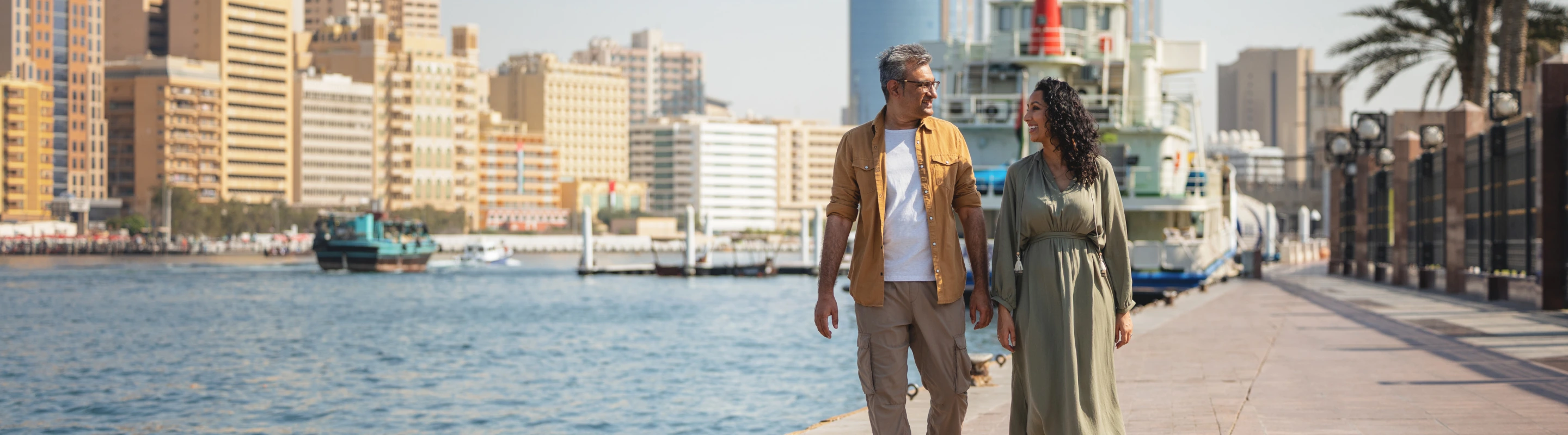 a middle eastern couple with travel insurance for the UAE enjoy a walk along Dubai Marina's waterfront