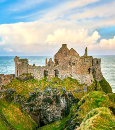 View of Dunluce Castle on a cliff overlooking the ocean, a place where people visit with travel insurance for Ireland
