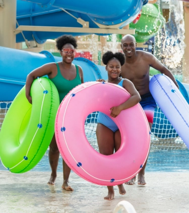 Parents with travel insurance for Florida at a waterpark with their daughter holding inner tubes at the bottom of a water slide