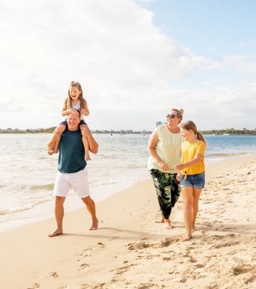 a family of four with travel insurance for Australia, enjoying a walk by the ocean together