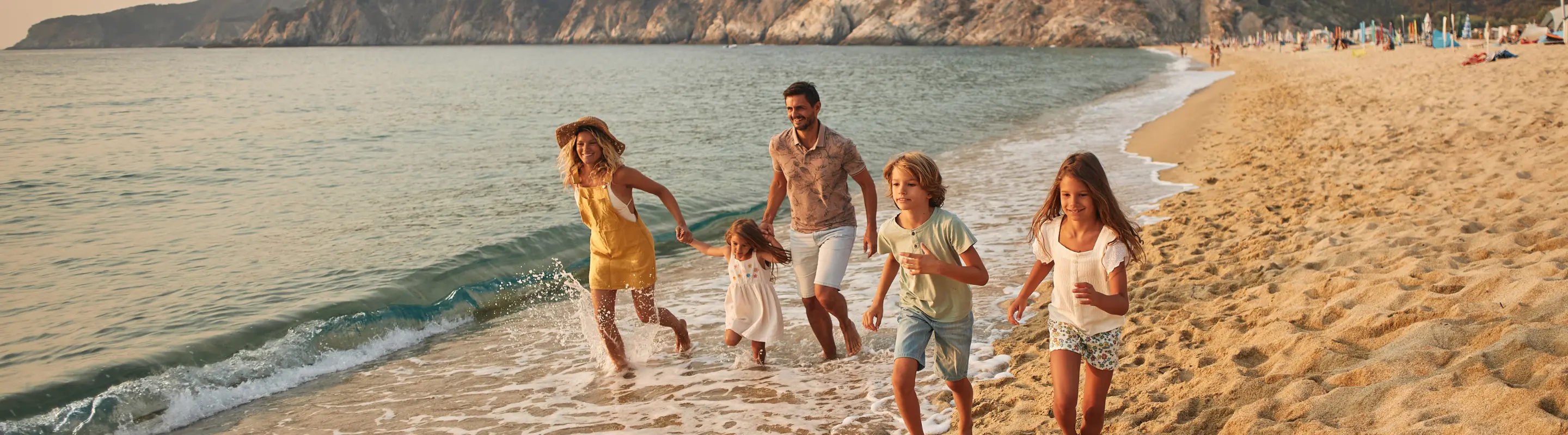 Parents with travel insurance for Greece running on the beach with their three children
