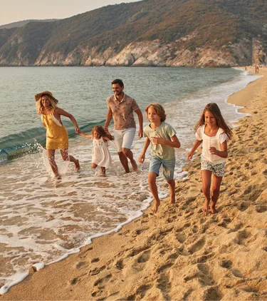 Parents with travel insurance for Greece running on the beach with their three children