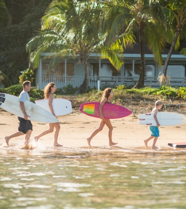 Parents and their three children with travel insurance for Hawaii walking on the beach with surfboards and boogie boards
