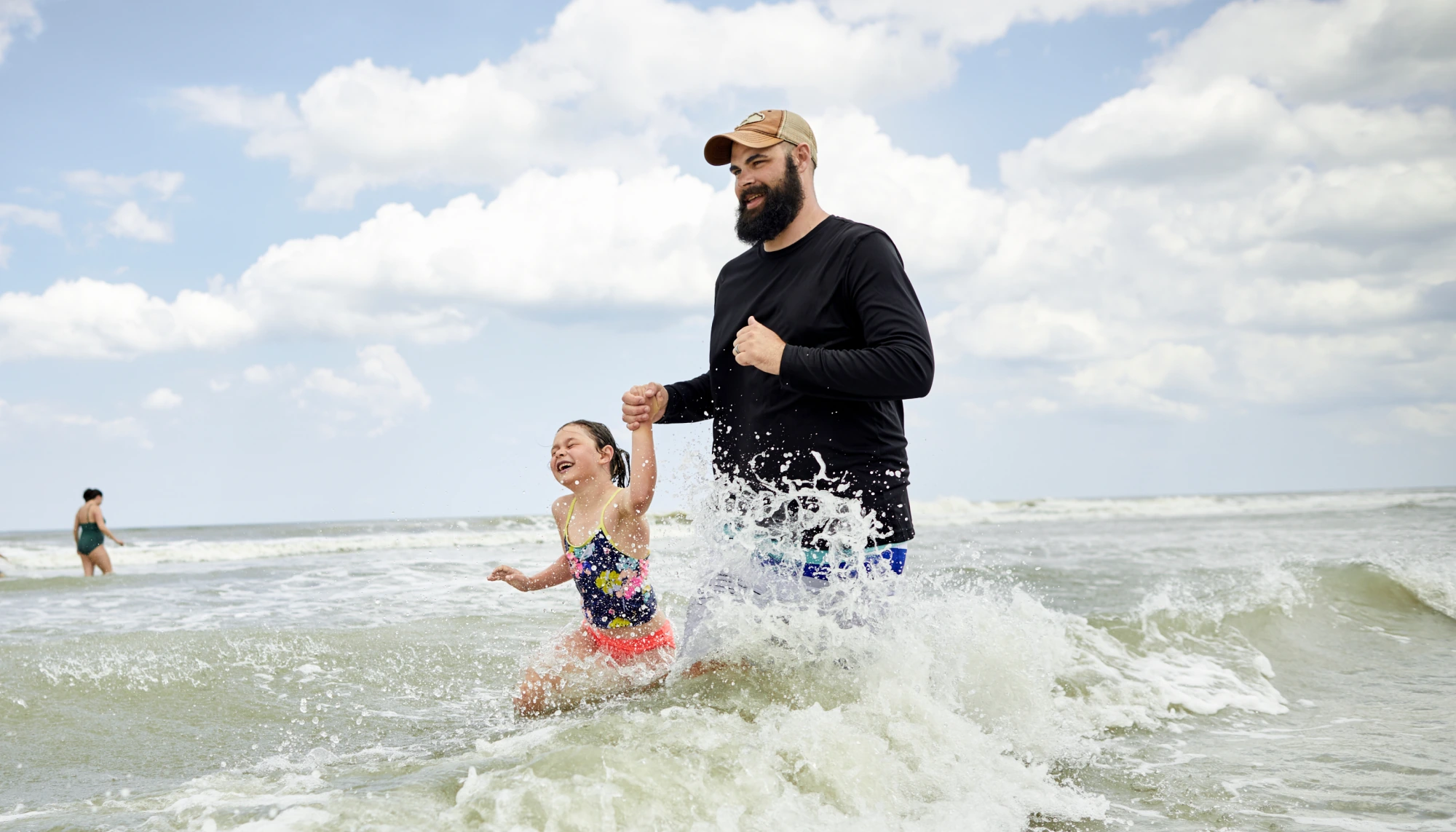 Father holding hands with his daughter and running in the ocean on vacation during hurricane season