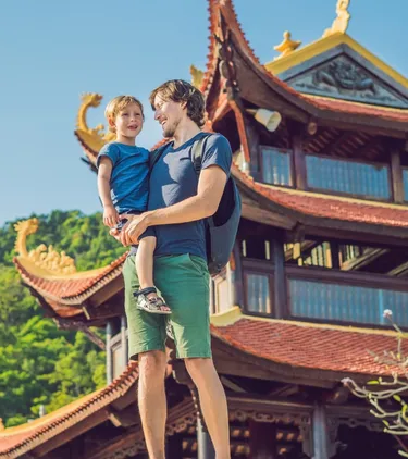 Father with travel insurance for Vietnam holding his son and smiling in front of a Buddhist temple in Phu Quoc
