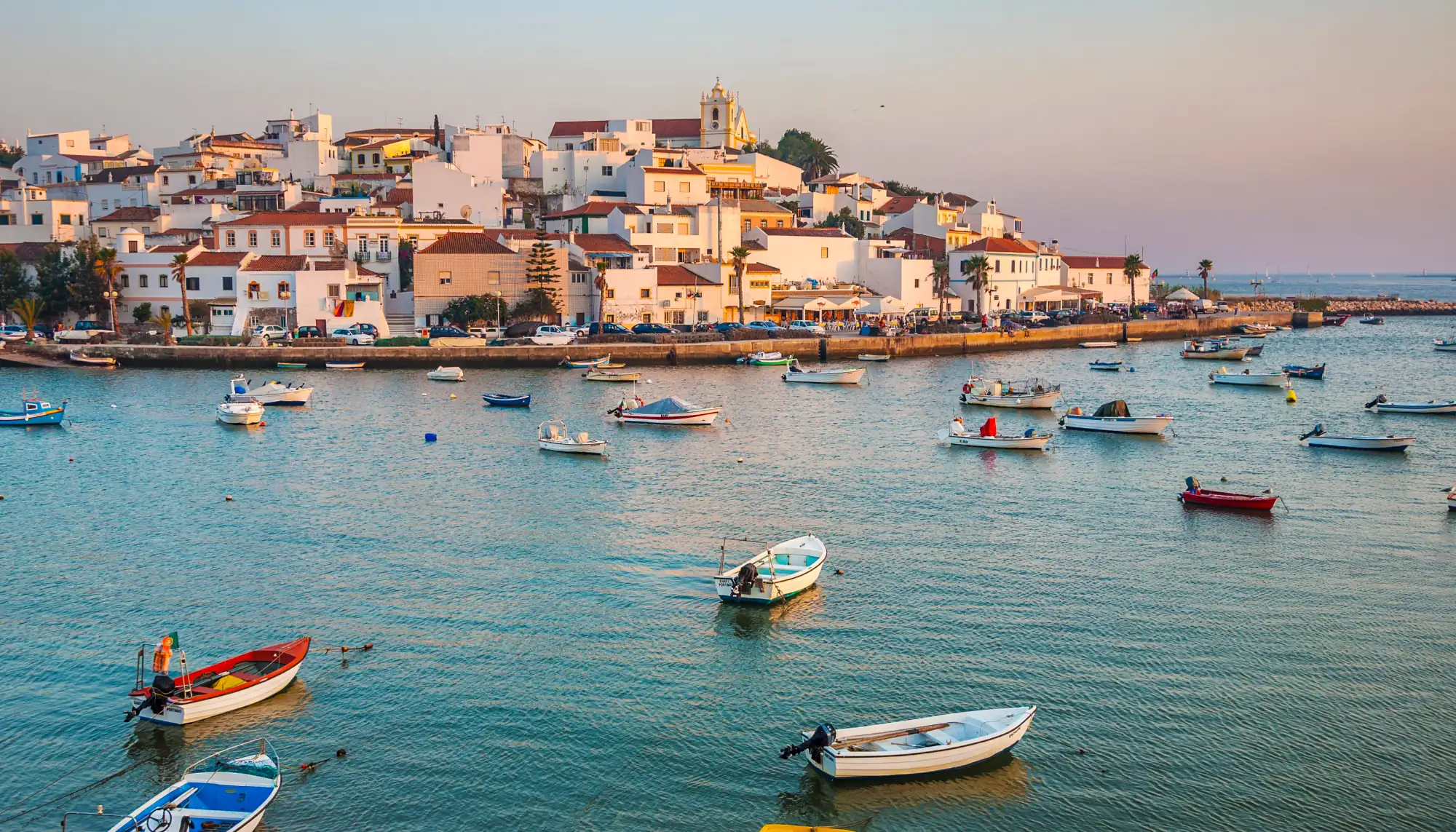 View of homes on a hill and boats in the water in Ferragudo, Portugal, highlighted in many Europe travel guides