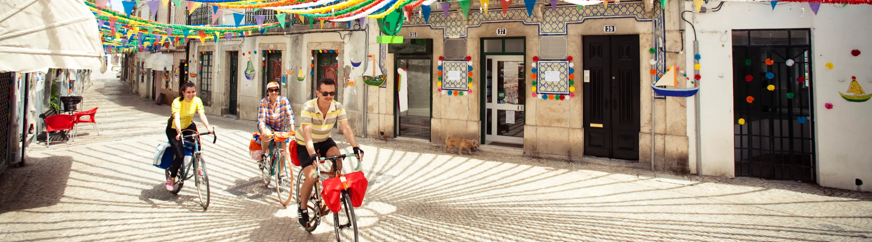 Friends biking on a colorfully decorated street in Alentejo with travel insurance for Portugal