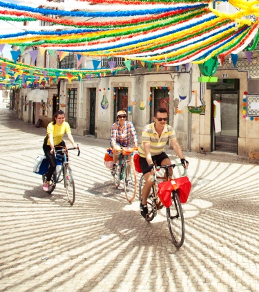 Friends biking on a colorfully decorated street in Alentejo with travel insurance for Portugal