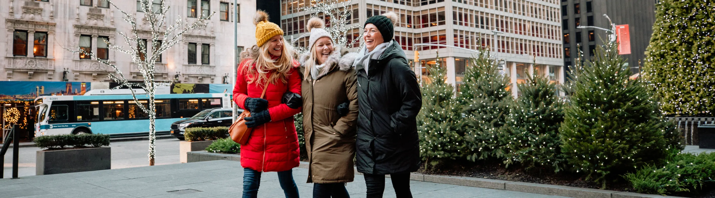 three women with travel insurance for New York, enjoying Christmas tree shopping in New York City