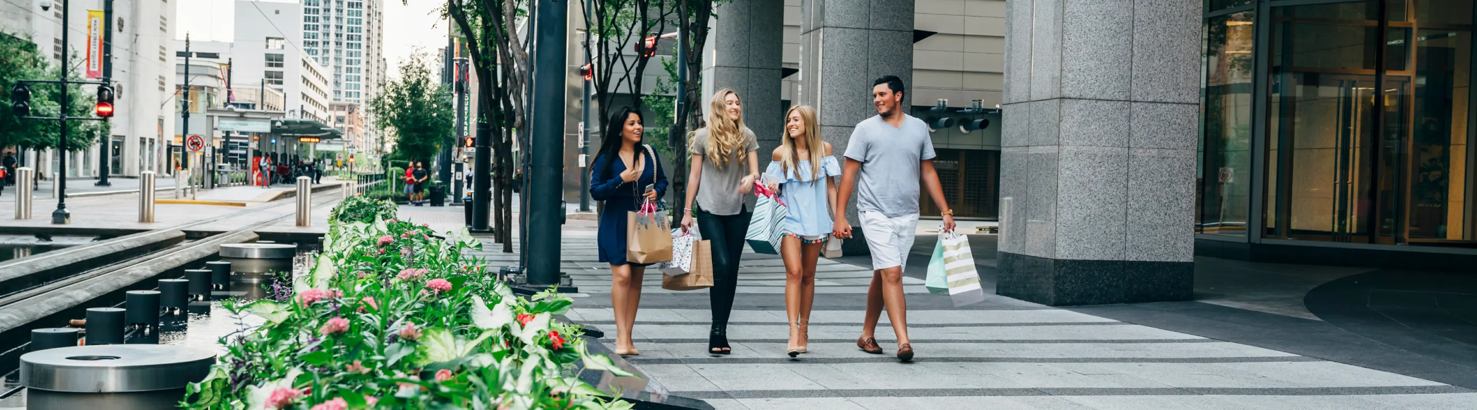 four friends hold shopping bags as they stroll through downtown Dallas on vacation with travel insurance for Texas