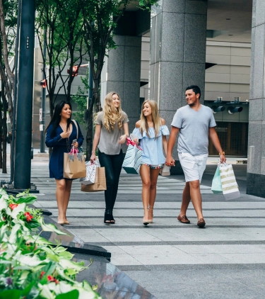 four friends hold shopping bags as they stroll through downtown Dallas on vacation with travel insurance for Texas