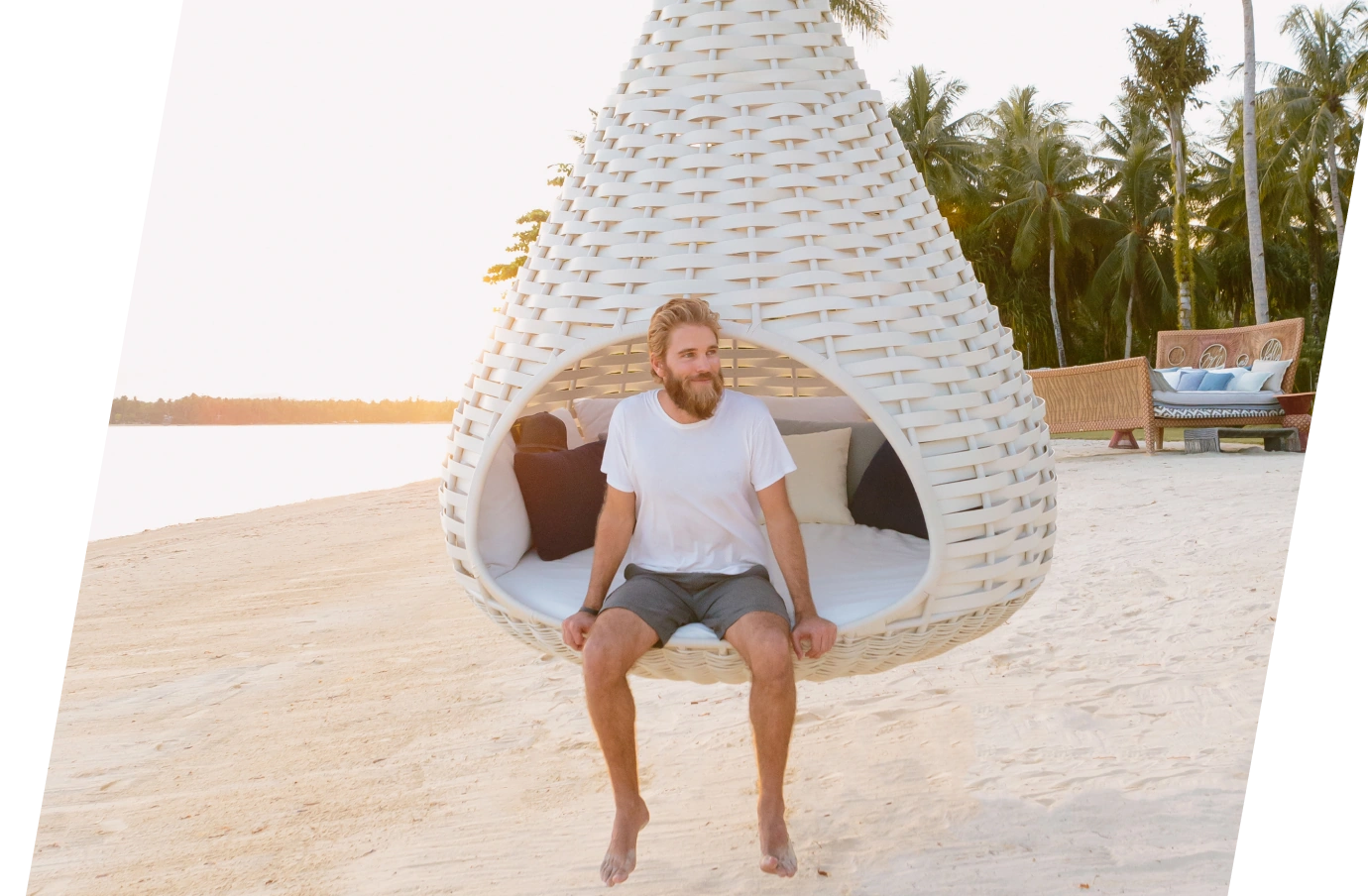 a man relaxing in a white, hanging basket chair on a beach, insured with travel insurance for the Philippines 