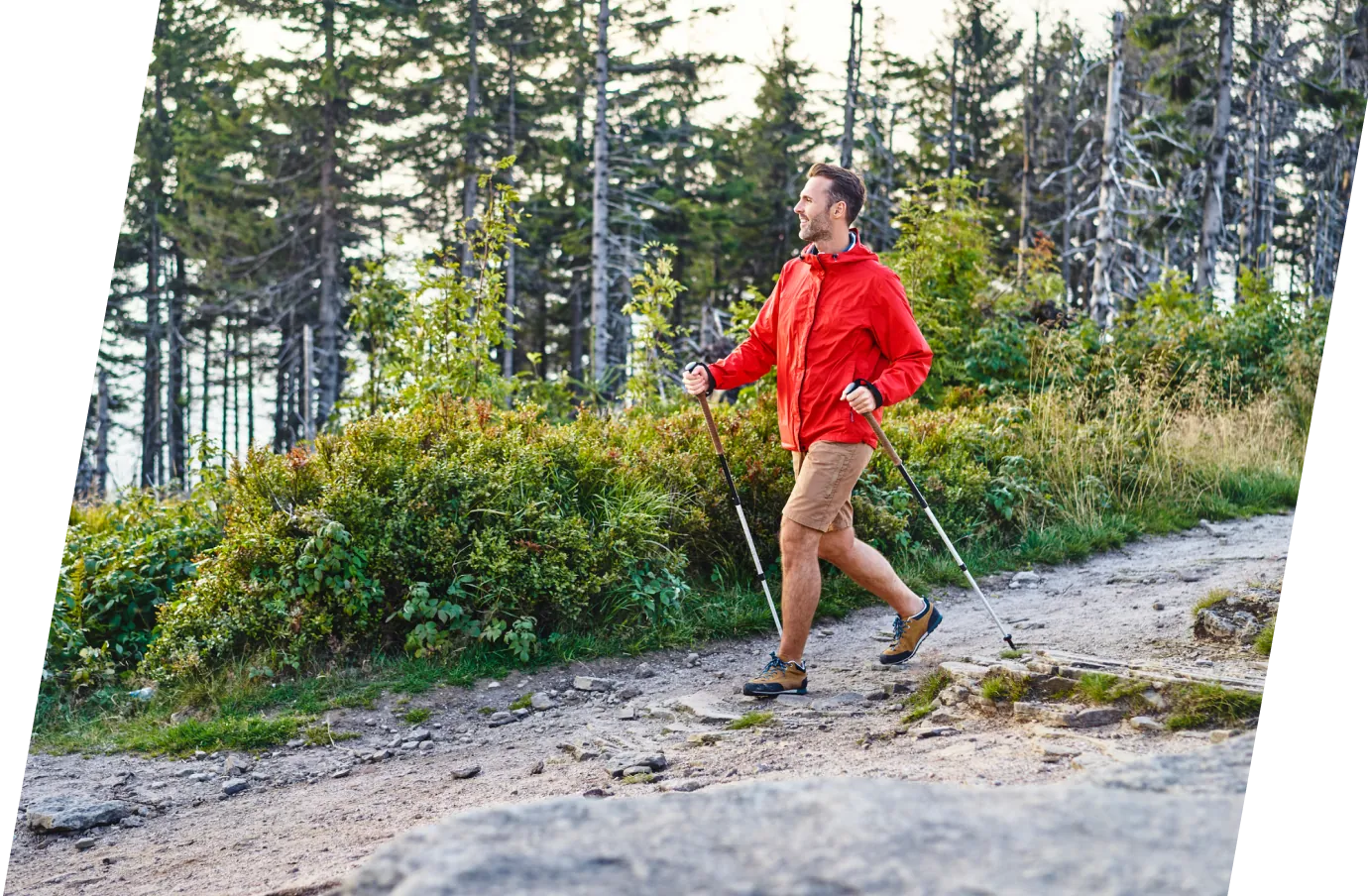 a young man wearing a red jacket and holding hiking poles hikes on a forest trail, insured with adventure travel insurance