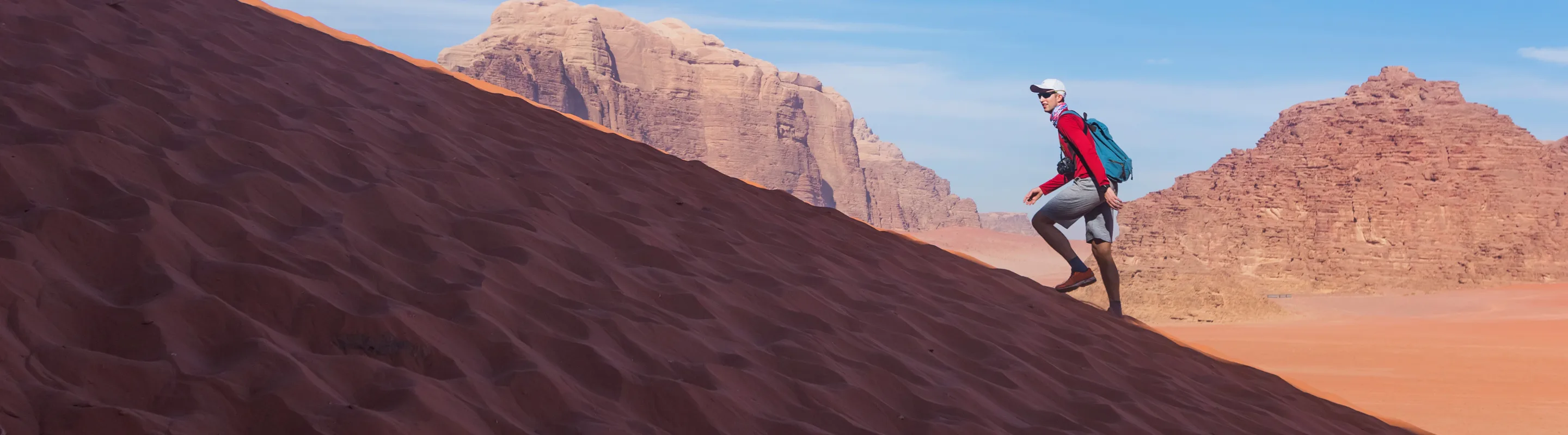 Man with travel insurance for Jordan hiking up a sandy hill in the desert