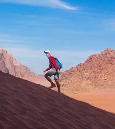 Man with travel insurance for Jordan hiking up a sandy hill in the desert