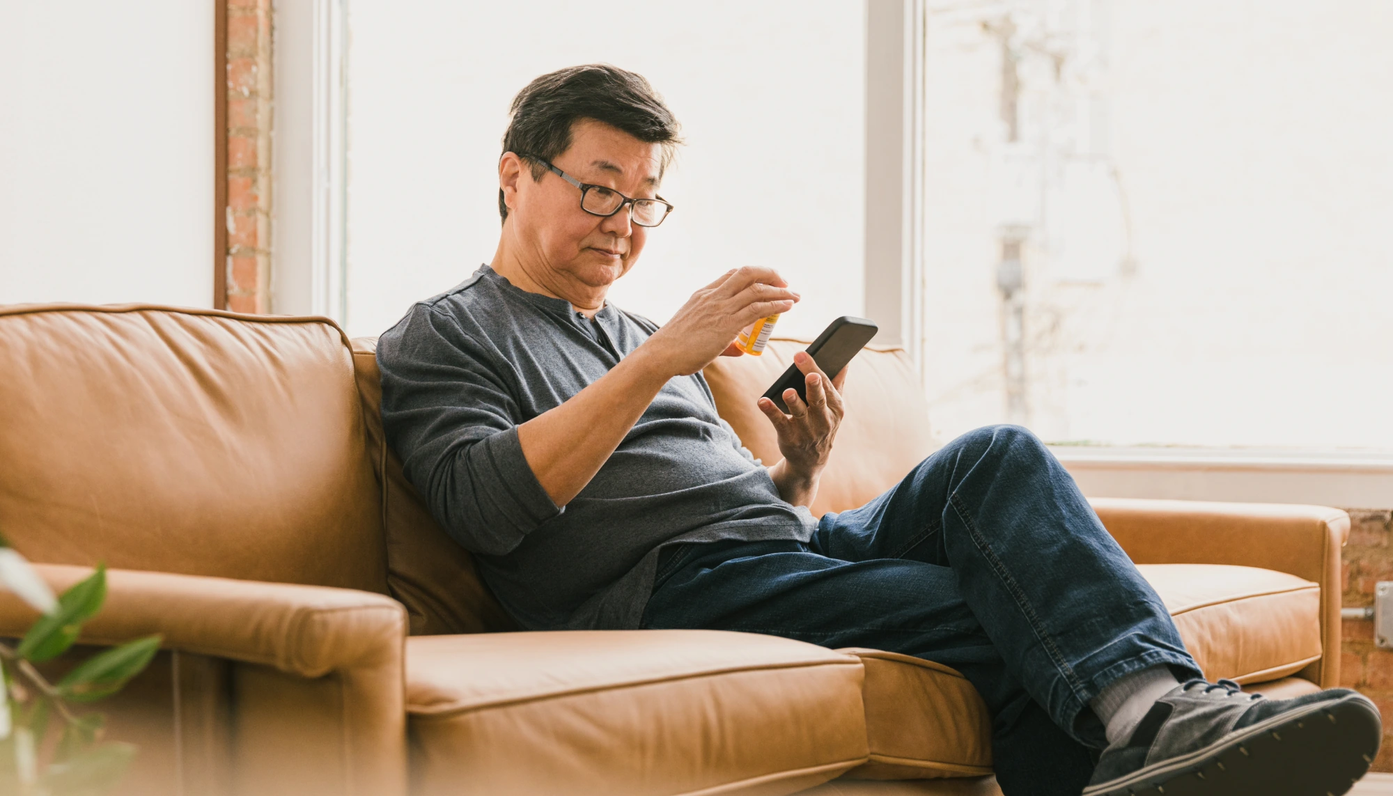 Middle-aged man looking at his prescription medication on vacation and holding his smartphone on the sofa